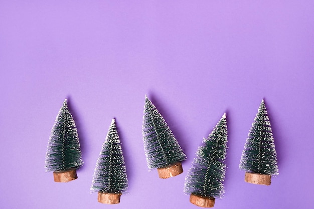 Small decorated christmas trees on purple background with copy space