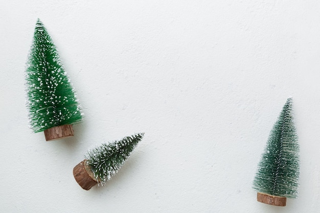 Small decorative Christmas trees with New Year decor on white putty background, top view