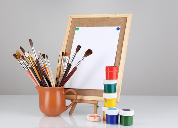 Small easel with sheet of paper and art supplies isolated on white