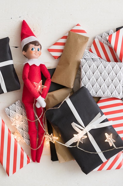 Small elf toy with Christmas gifts lights and advent calendar presents on white wooden background