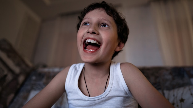 Foto piccolo ragazzo emotivo, felice con un ampio sorriso, guarda la tv a tarda notte