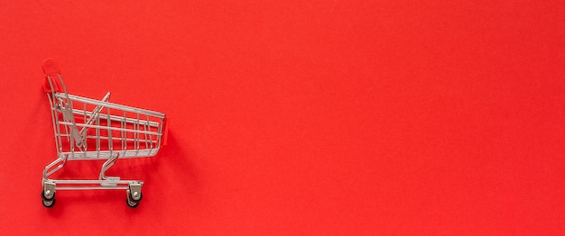 Small empty shopping trolley cart on red background. 