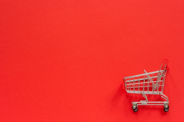 Small empty shopping trolley cart on red 