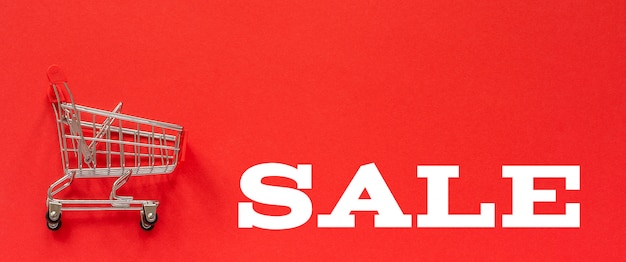 Foto piccolo carrello del carrello dello shopping vuoto e testo vendita su sfondo rosso.