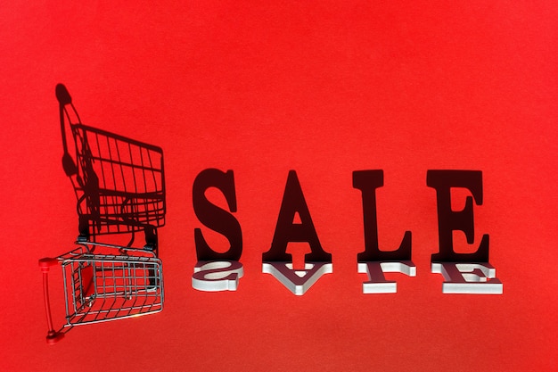 Small empty shopping trolley cart and word SALE of white letters casts a large shadow 