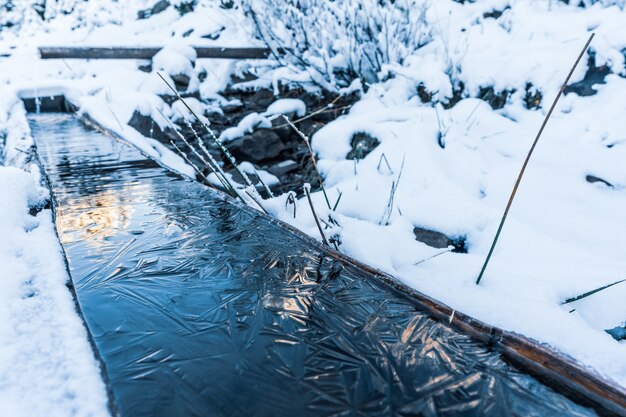 A small fast spring with clean cool transparent water among heavy snow and dark forest in the picturesque Carpathian mountains