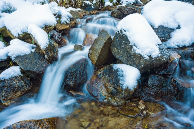 Small fast stream among small wet stones and cold white snow in the picturesque Carpathian mountains in beautiful Ukraine and its fantastic nature