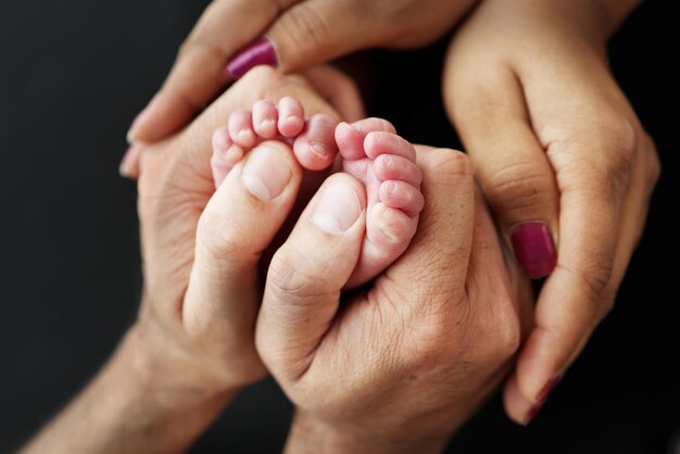 small feet of a newborn in the hands of parents loving palms of the hands of mother and father conceptual image of fatherhood closeup selective focus professional photography a black background