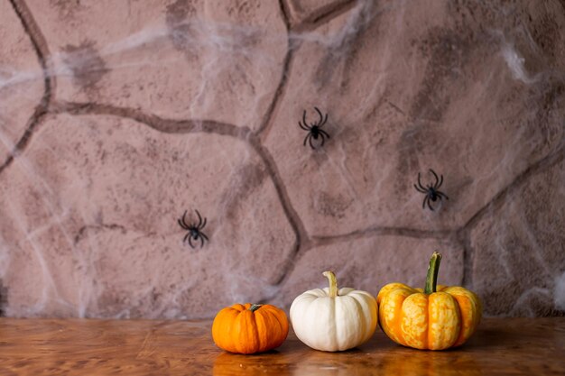 Small festive pumpkins lie on the table with a bouquet of yellow ears and spiders on the wall