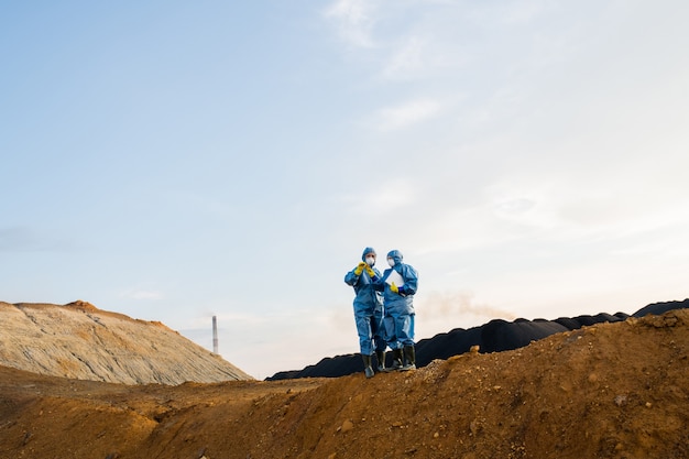 Small figures of two female researchers standing on top of hill during investigation of abandoned territory with polluted soil and air