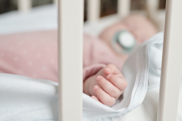 Small fingers and hand of baby girl sleeping in crib