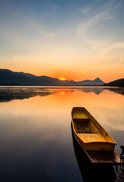 山と日の出の夕暮れの空と湖の小さな漁師のボート