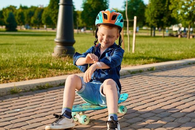 small fiveyearold boy in helmet fell off skateboard injured hand and is sealing it with a plaster