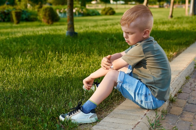 Photo small fiveyearold redhaired boy is sitting on road in park and gluing wound on elbow