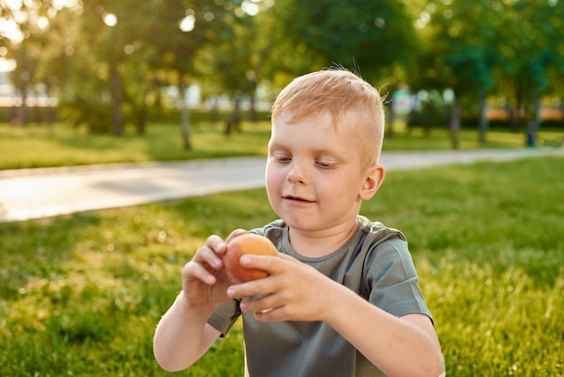 small fiveyearold redhaired boy looks at peach is about to eat it in park