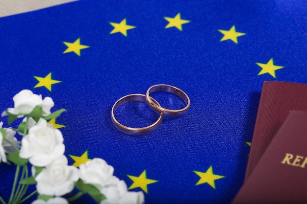 Small flag of the European Union flowers,passes and marriage rings on a white surface.