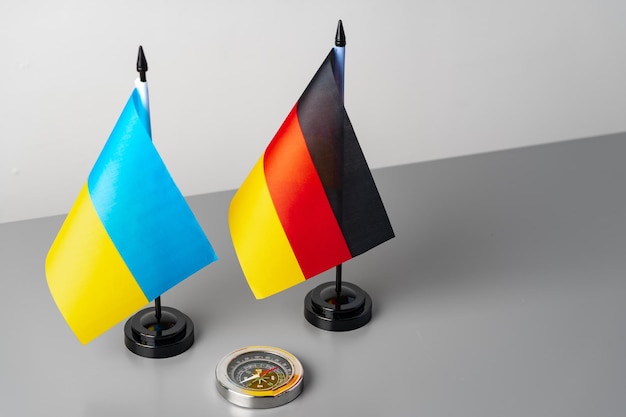 Small flags of ukraine and germany on gray background with compass