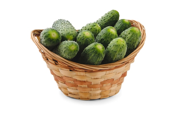 Small fresh green cucumbers are stacked vertically in a tall beige wicker basket, isolated on white with a shadow.