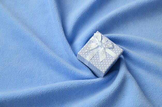 A small gift box in blue with a small bow lies on a blanket of soft 