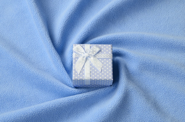 Маленькая подарочная коробка синего цвета с маленьким бантиком лежит на одеяле