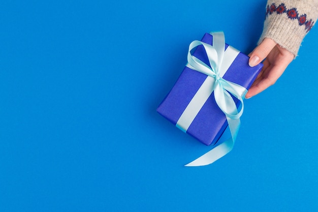 Small gift box in female hands on blue , view from above