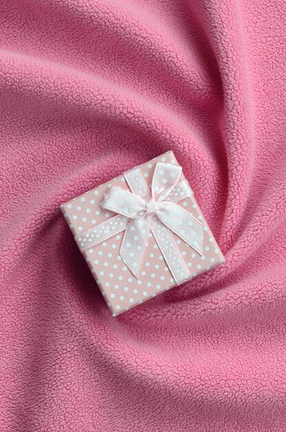 A small gift box in pink with a small bow lies on a blanket