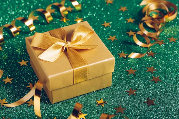 Small gift box with golden bow on green glitter background