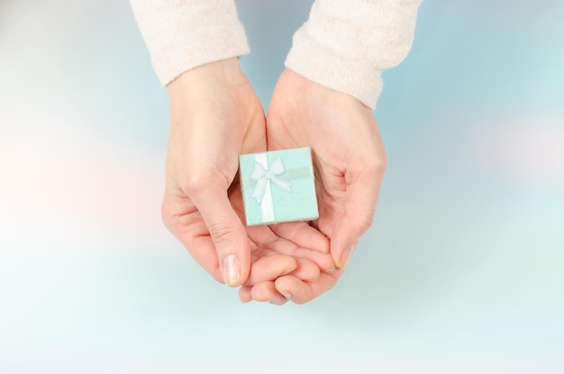 Small gift box in women\'s hands hands holding small gift with\
blue ribbon