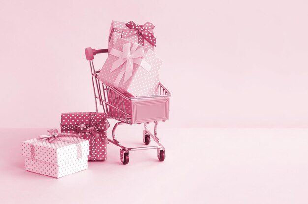 Small gift boxes of different colors with ribbons in shopping cart on a violet and blue pastel background Image toned in Viva Magenta color of the 2023 year