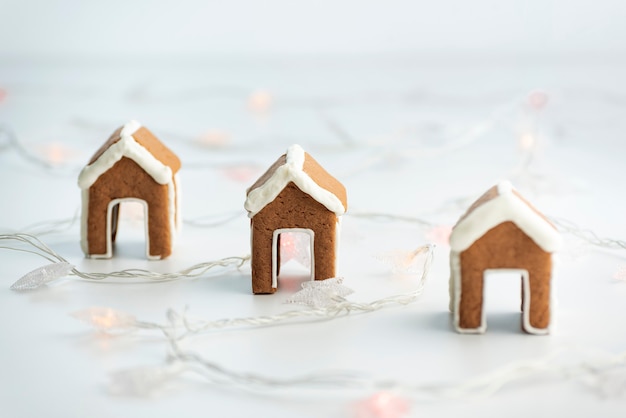 Small gingerbread houses for a cup on white background next to garland. Christmas baked goods.