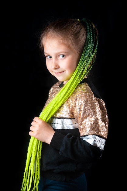 A small girl on a black background with green Afro elastic bands pigtails tied in a ponytail