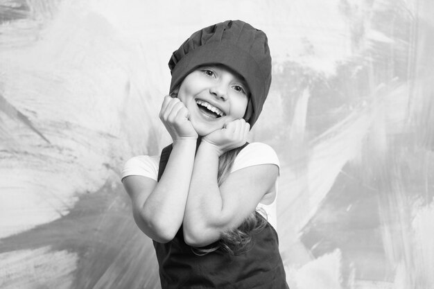 Маленькая девочка-повар со счастливым лицом в шляпе и фартуке