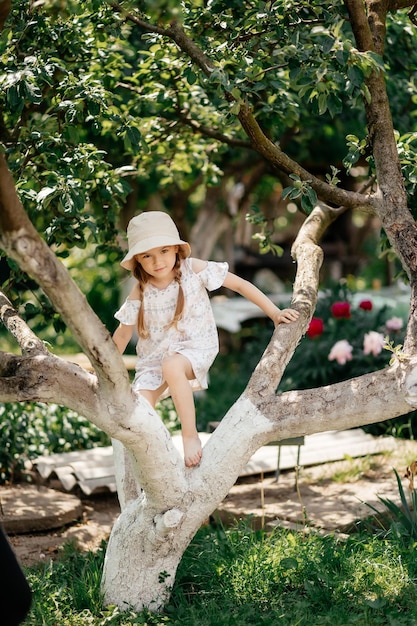 Small girl climb tree in summer garden activity Little girl on tree branch childhood Vacation activity lifestyle Kid fashion style beauty Childhood youth growth