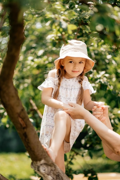 Small girl climb tree in summer garden activity Little girl on tree branch childhood Vacation activity lifestyle Kid fashion style beauty Childhood youth growth