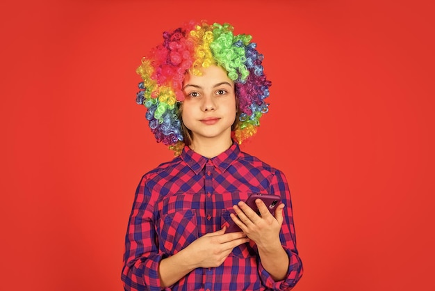Small girl colorful wig use smartphone positive and cheerful\
childhood happiness kid looking funny in rainbow wig hair hair\
dyeing at hairdresser child having fun happy birthday party