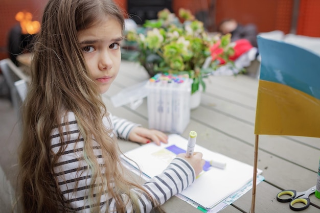 Small girl draws ukrainian flag in safe place abroad in europe where she fled from russian invasion