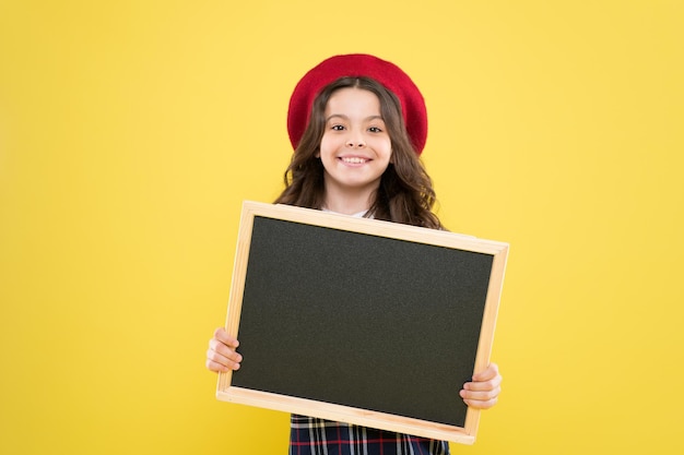 Piccola ragazza in berretto francese pubblicità bambino con lavagna vuota bambino parigino su sfondo giallo ragazza felice con i capelli ricci in berretto la tua pubblicità in buone mani scheda pubblicitaria