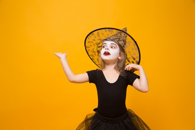 Small girl in Halloween witch costume, orange surface.