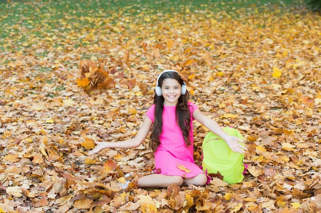 small girl having fun with autumn leaves after school fall time