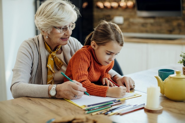 Small girl and her grandmother drawing on the paper at home