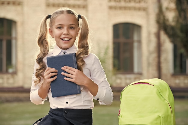 Фото Маленькая девочка держит в руках книжную литературу для детей, развивающая детство, работает с ноутбуком обратно в школу ребенок со школьной сумкой улыбающийся ребенок с рюкзаком позволяет делать домашнее задание