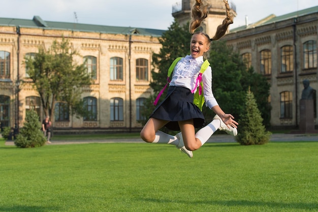 Small girl jump with backpack. happy to be here. happy childhood memories. end of lesson. back to school. kid study in park. relax on green grass with school bag. education concept. key to success.