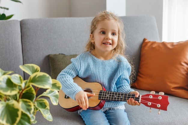 Piccola ragazza che suona l'ukulele e canta a casa. chitarra di apprendimento del bambino. educazione della prima infanzia