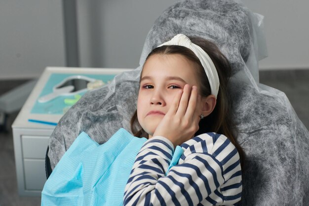 Photo small girl pointing at painful tooth site during appointment with his dentist at dental clinic.