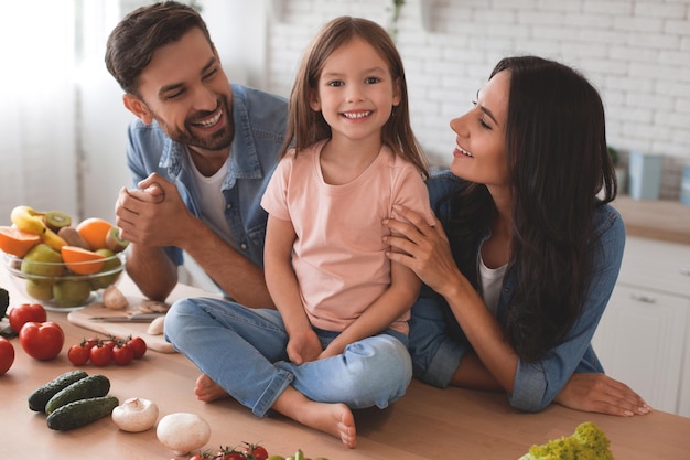 Small girl sitting on the kitchen table with parents looking at her