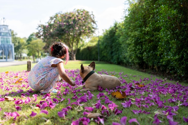 Small girl sitting with french bulldog at field.