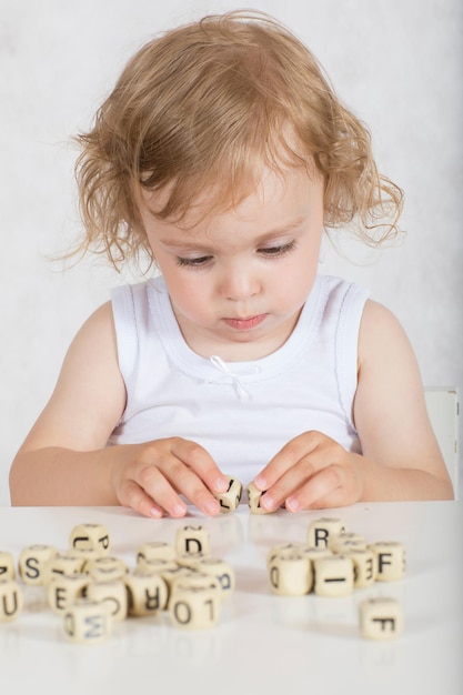 Small girl of two years composes words from letters. Closeup