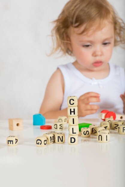 Small girl of two years composes words from letters. Closeup