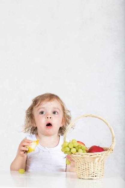2년 된 어린 소녀가 테이블에서 신선한 과일을 먹고 있습니다. 확대