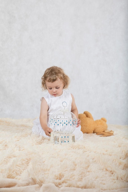 Small girl of two years old  in a white dress is playing with her toys.